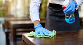 Close-up of waitress disinfecting tables at outdoor cafe during coronavirus epidemic.