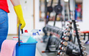 Gym cleaning concept. Cleaning lady stands with a bucket and cleaning products on the background of the gym.