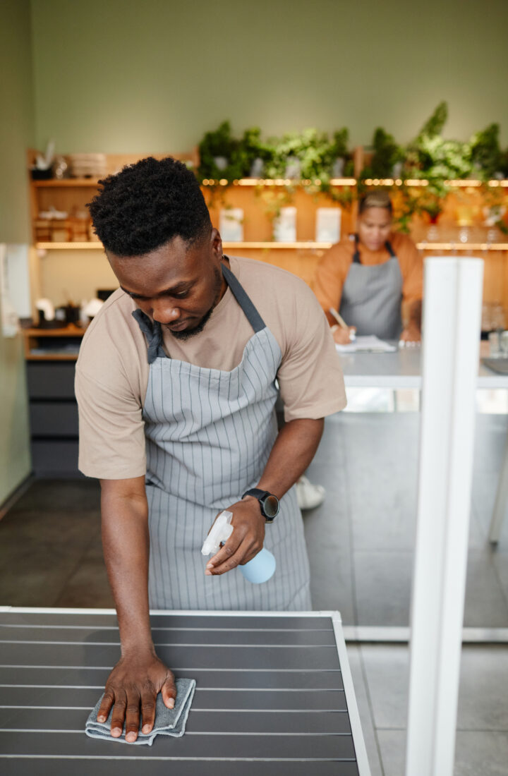 Vertical shot of modern young cafe workers starting workday with cleaning furniture and making notes