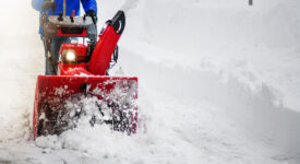 Man clearing or removing snow with a snowblower on a snowy road detail.