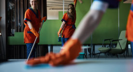 Three janitors doing the cleaning in the office cafe Smiling cute cleaner with a mop in her hands posing for the camera in the presence of her busy colleagues