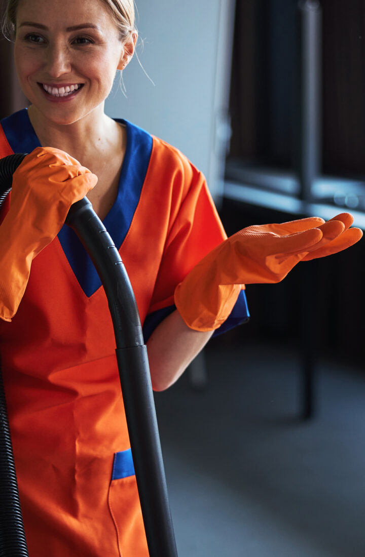 Beautiful joyous professional female janitor in the uniform and rubber gloves talking to her colleagues