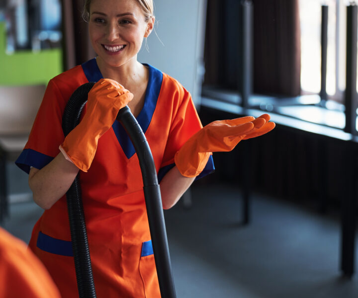 Beautiful joyous professional female janitor in the uniform and rubber gloves talking to her colleagues