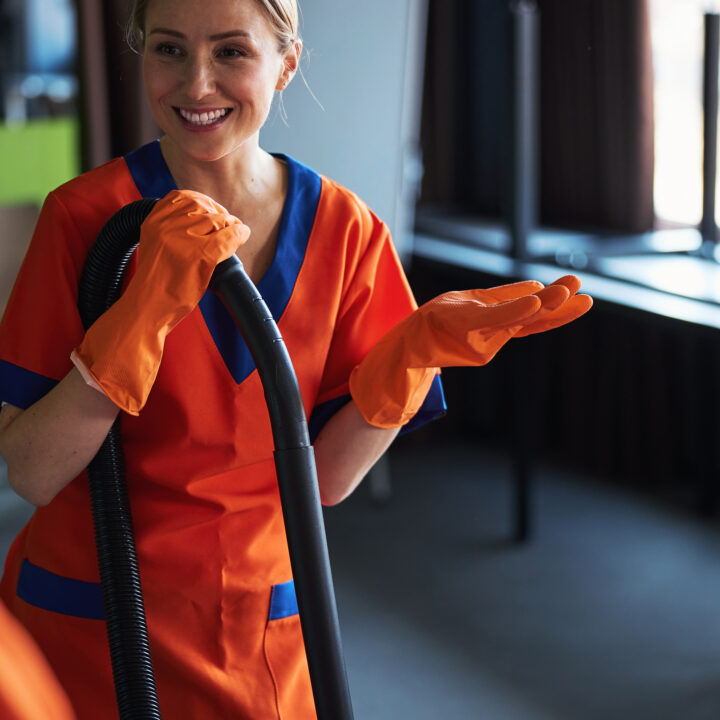 Beautiful joyous professional female janitor in the uniform and rubber gloves talking to her colleagues