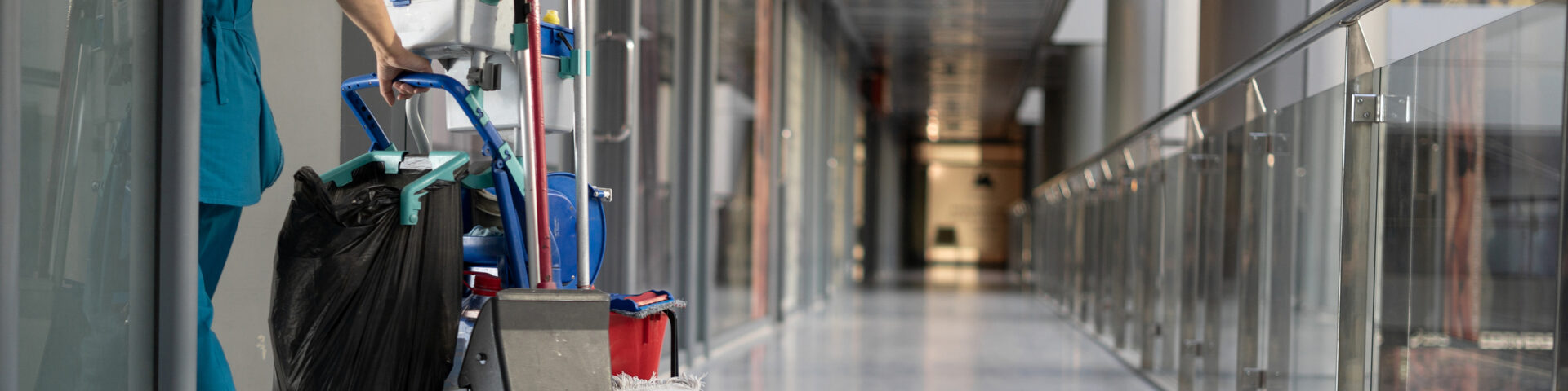 An employee pulls a trolley for cleaning offices. Woman cleaner is engaged in work. Shopping center place for text