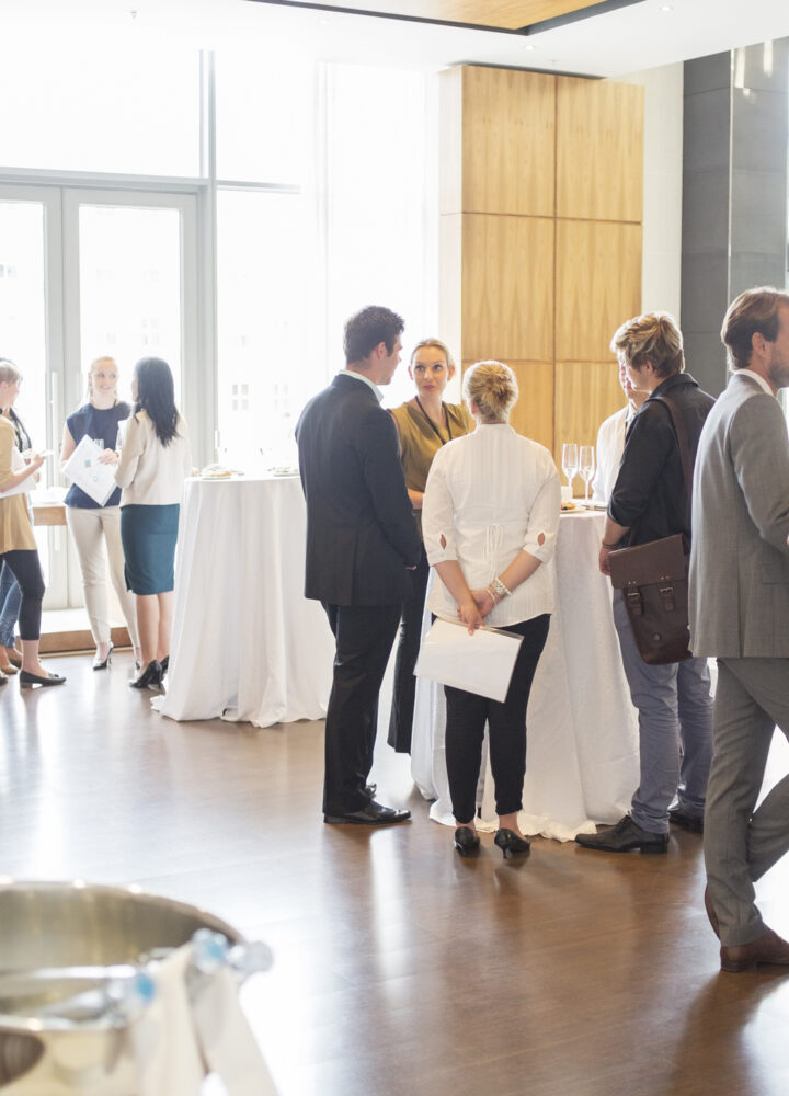Group of conference participants standing in lobby of conference center, socializing during lunch break